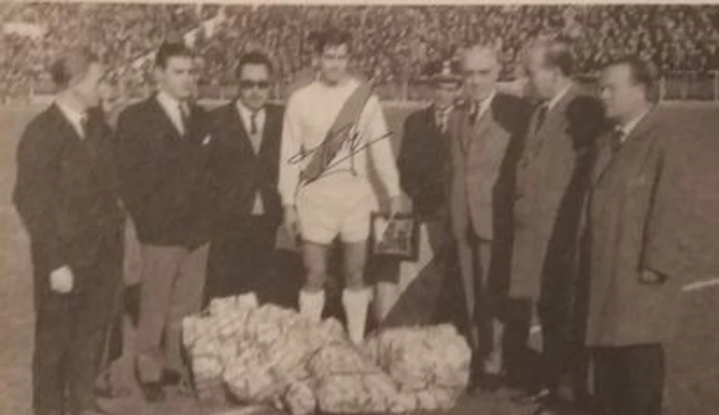 Капитан команды Флорес и представителями магазинов Прогресо и представителем болельщиков получает наградную табличку за достижения в спорте, у его ног подарки команде